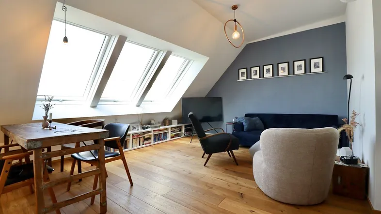 Helles Wohn- und Esszimmer im Dachgeschoss mit Holzboden, schrägen Wänden und großen Dachfenstern.