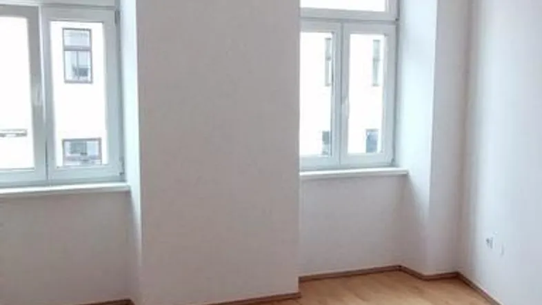 Helles Wohnzimmer mit Holzboden und hohen Decken, durch große Fenster lichtdurchflutet.