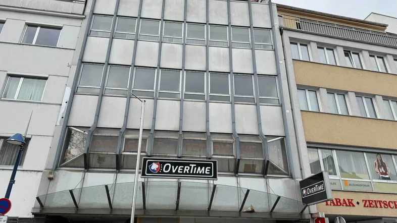 Fassade eines Geschäftsgebäudes mit großen Fenstern und einem "Overtime"-Schild an der Vorderseite.