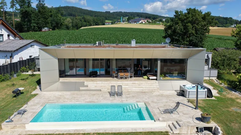 Moderne Villa mit großem Außenpool und Whirlpool, umgeben von grüner Landschaft und Feldern.