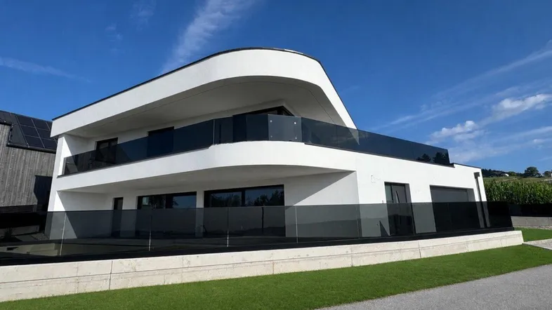 Elegante moderne Villa mit weißer Fassade, dunklen Glasgeländern und weitem Blick in die Landschaft.