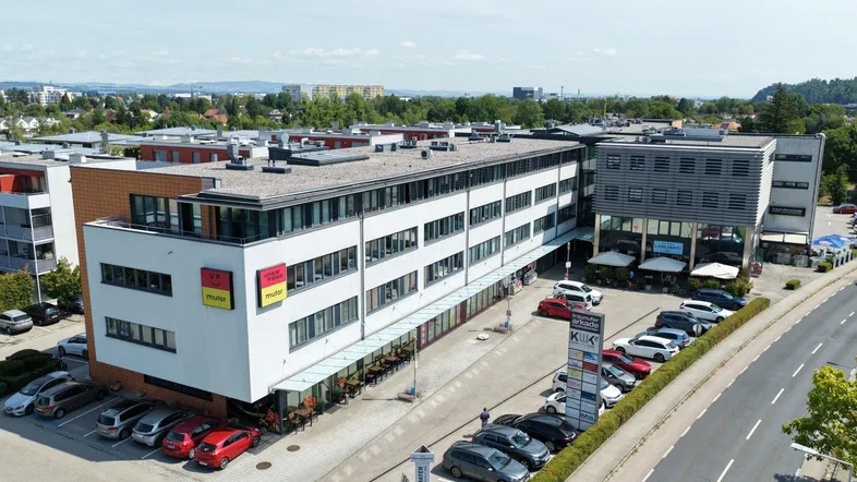 Luftaufnahme eines modernen Büro- und Geschäftsgebäudes mit Parkplätzen und umliegender Infrastruktur.