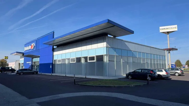 Modernes Geschäftsgebäude mit blauer Fassade und großem Parkplatz unter klarem Himmel.