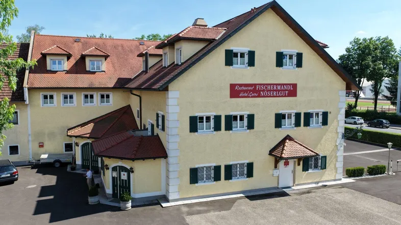 Traditionelles Gebäude mit gelber Fassade, grünen Fensterläden und rotem Dach in sonniger Umgebung.