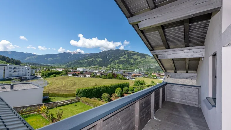Balkon mit Holzboden und Geländer, bietet einen weiten Blick auf die umliegende Berglandschaft und grüne Felder.