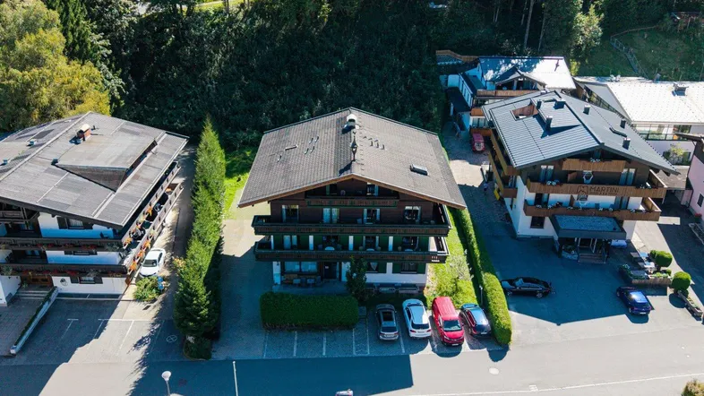Luftaufnahme eines Mehrfamilienhauses mit traditioneller Architektur, umgeben von Parkplätzen und Bäumen.