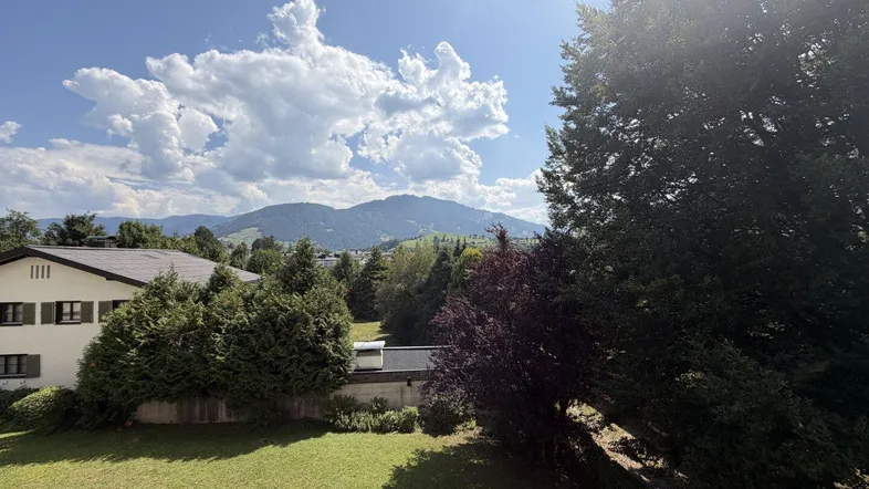 Panoramablick auf die umliegende Berglandschaft mit viel Grün und einem sonnigen Himmel.