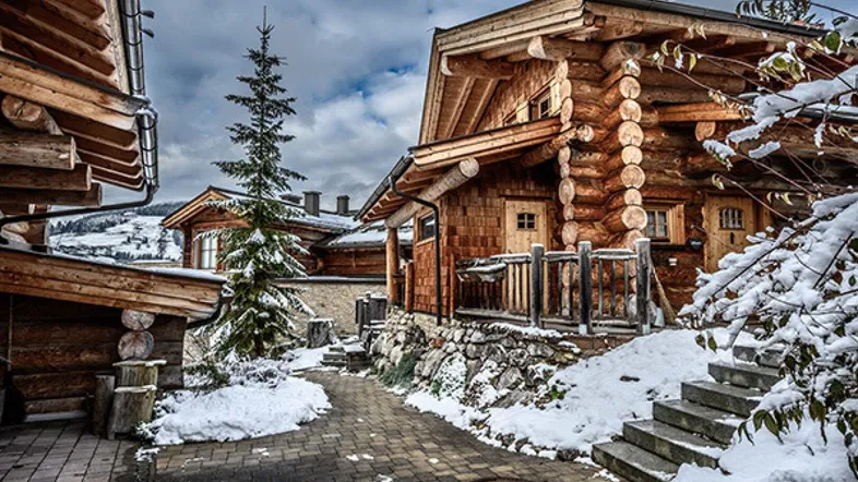 Winterliche Ansicht eines traditionellen Holzhauses mit verschneitem Dach und Wegen in den Bergen.