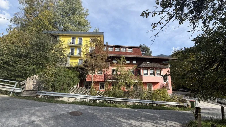 Mehrere Gebäude in einer bergigen Landschaft mit Bäumen und einer Straße im Vordergrund, die zum Anwesen führt.