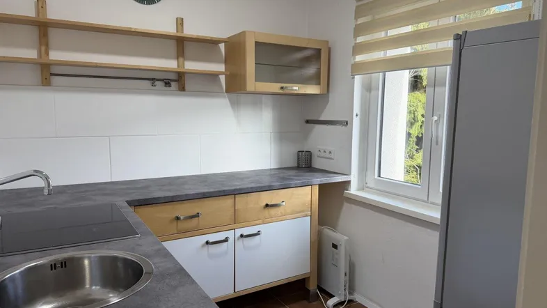 Funktionale Küche mit Induktionskochfeld, Spüle, Holzschränken und einem Fenster mit Jalousien.