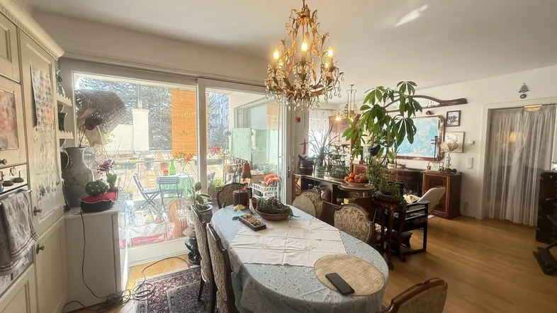 Helles Esszimmer mit Kronleuchter, Holzboden und Zugang zu einem sonnigen Balkon.