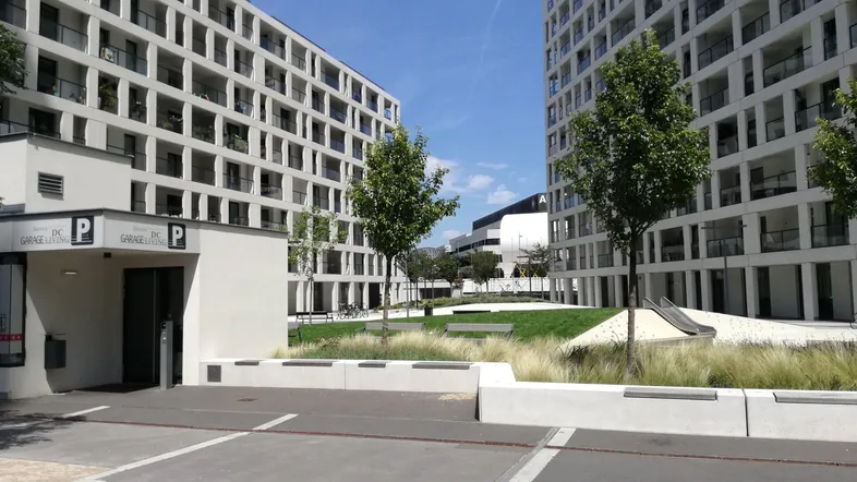Moderne Wohngebäude mit Tiefgarageneinfahrt und begrüntem Innenhof unter blauem Himmel.