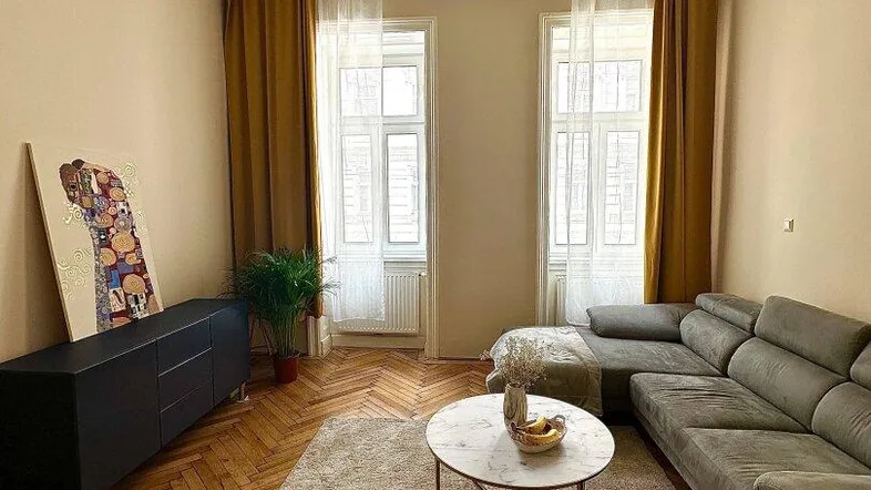 Helles Wohnzimmer mit Fischgrätparkett, großem Sofa, Kronleuchter und hohen Fenstern.