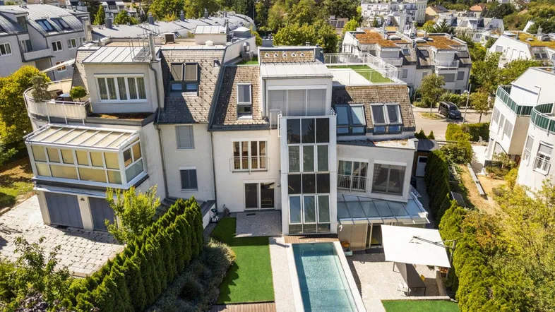 Luftaufnahme einer modernen Villa mit Pool, Garten und umliegender Wohnbebauung unter blauem Himmel.