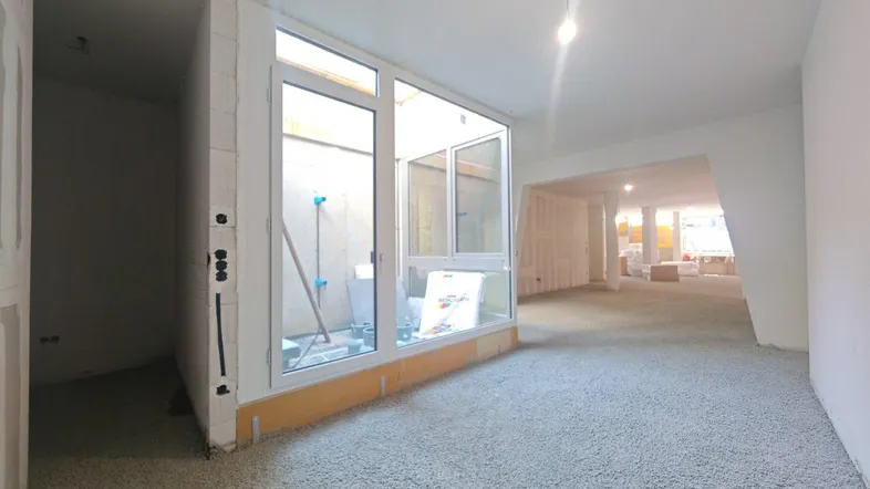 Unfertiger Innenraum mit großen Fenstern und Rohbauzustand, bereit für den weiteren Ausbau.