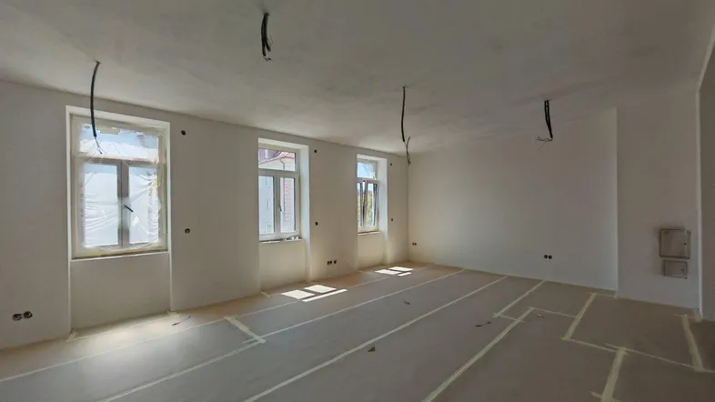 Heller Raum im Rohbau mit frisch verputzten Wänden und mehreren Fenstern, bereit für den Innenausbau.