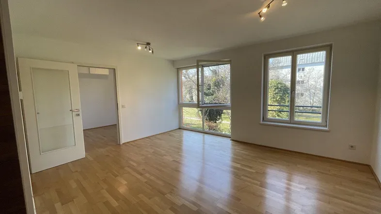 Helles Wohnzimmer mit Parkettboden und großen Fenstern, die einen Blick ins Grüne bieten.