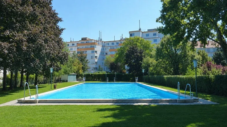 Großer Gemeinschaftspool mit gepflegter Rasenfläche und Wohngebäuden im Hintergrund.