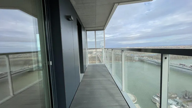 Langer Balkon mit Glasgeländer und weitem Blick auf den Fluss und die Stadt.