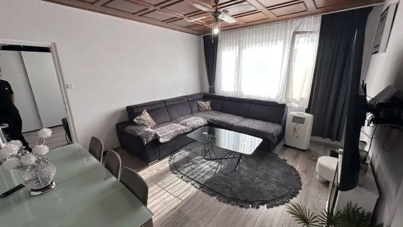 Geräumiger Wohn-Essbereich mit dunklem Ecksofa, Esstisch und einer auffälligen Holzdeckenvertäfelung.