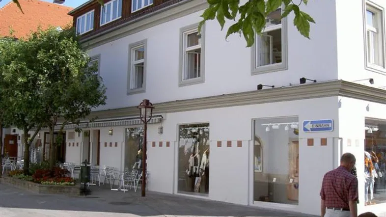 Weißes Geschäftsgebäude mit großen Schaufenstern und Außenterrasse in einer belebten Straße.