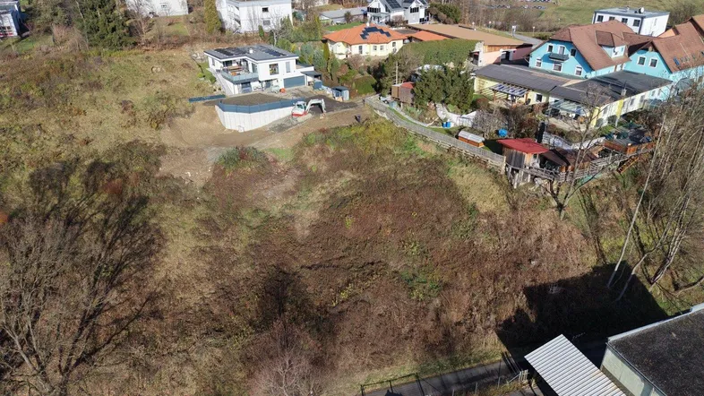 Luftaufnahme eines unbebauten Hanggrundstücks mit umliegenden Häusern und Blick auf die Stadt.