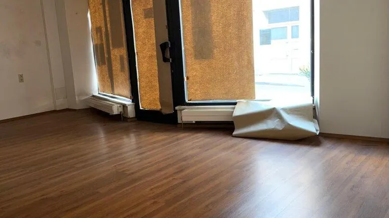Heller, leerer Geschäftsraum mit großen Schaufenstern und Laminatboden, bereit zur individuellen Gestaltung.