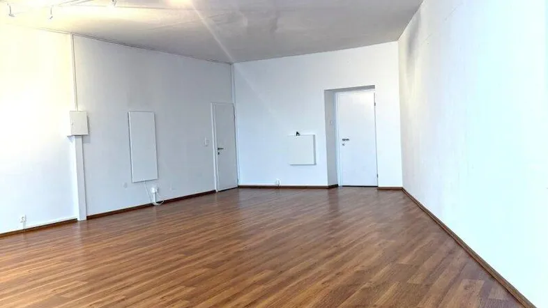Geräumiger, leerer Raum mit hellem Laminatboden und weißen Wänden, ideal für gewerbliche Nutzung.