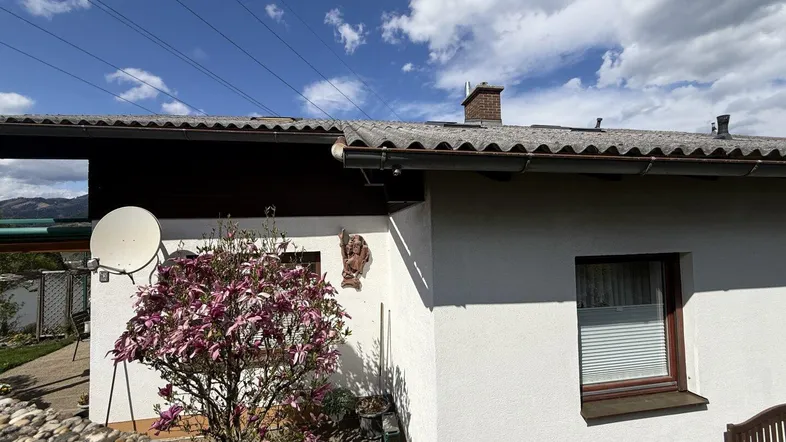 Teilansicht des Hauses mit blühendem Strauch und Satteldach unter blauem Himmel.