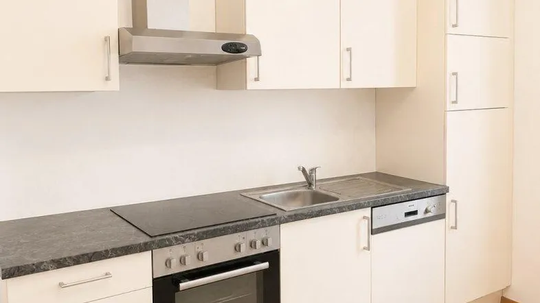 Moderne Einbauküche mit hellen Schränken, dunkler Arbeitsplatte und integrierten Geräten.