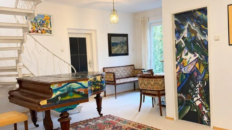 Geräumiges Wohnzimmer mit Wendeltreppe, Flügel und farbenfrohem Teppich, hell und einladend.