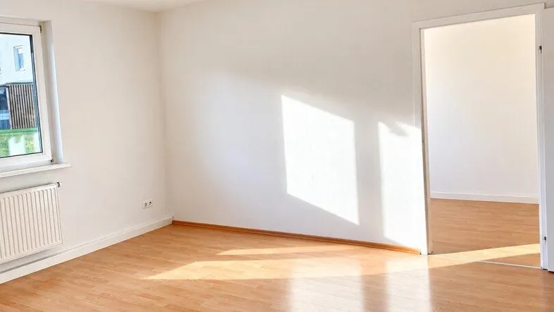 Helles, leeres Zimmer mit Laminatboden und weiß gestrichenen Wänden, bereit zum Einzug.