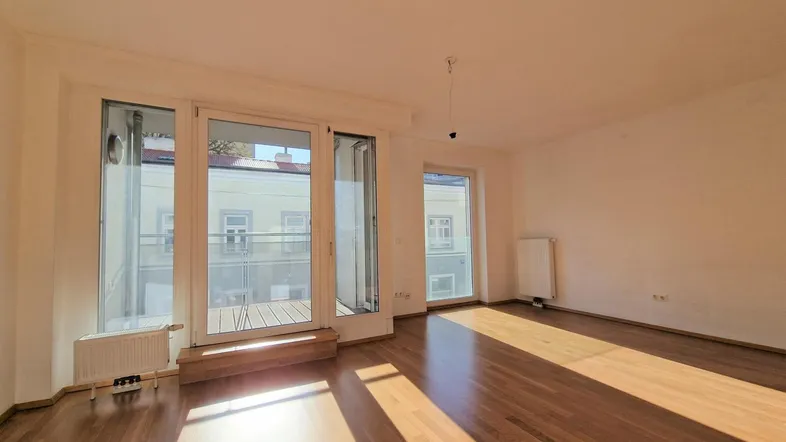 Helles Wohnzimmer mit Parkettboden und Zugang zu einem sonnigen Balkon.