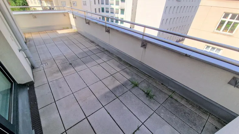 Geräumige Terrasse mit Fliesenboden und Blick auf die umliegenden Gebäude der Stadt.
