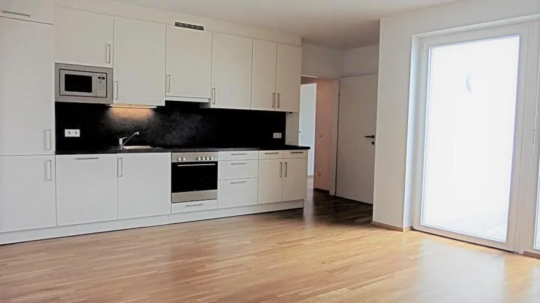 Moderne Einbauküche in einem offenen Wohnbereich mit Parkettboden und Zugang zum Balkon.