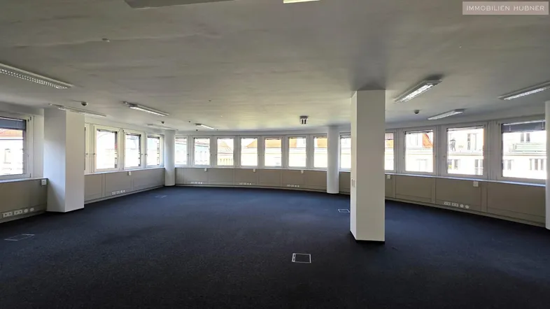 Großes, offenes Büro mit Teppichboden, vielen Fenstern und Säulen, ideal für flexible Arbeitsplatzgestaltung.