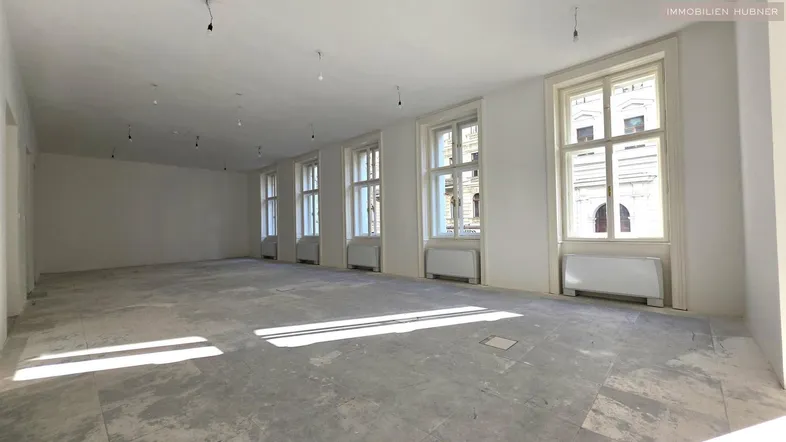 Großer, heller Raum mit vielen Fenstern und Betonboden, bereit für den Ausbau.