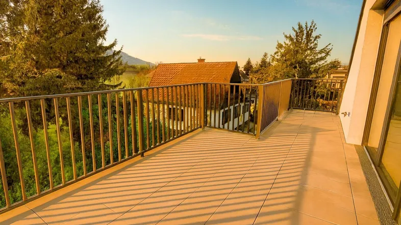 Große geflieste Terrasse mit Metallgeländer und weitem Blick auf die umliegende Landschaft und Berge.