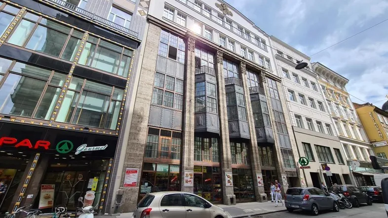 Ansicht der historischen Fassade eines Geschäftsgebäudes an einer belebten Straße mit parkenden Autos und Geschäften.