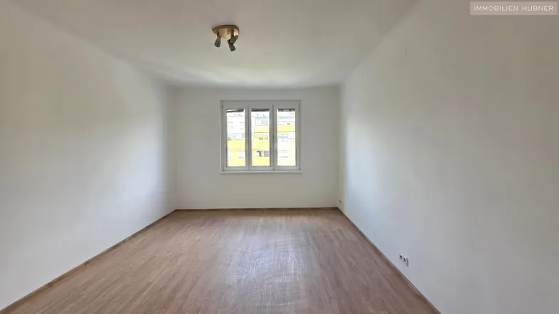 Helles, leeres Zimmer mit Laminatboden und Fenster, bereit zur individuellen Gestaltung.