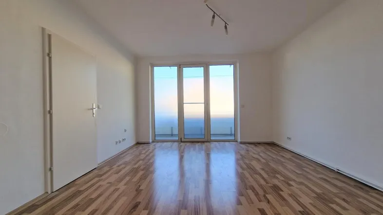 Heller Wohnraum mit Holzparkettboden und Zugang zu einem Balkon oder einer Loggia.