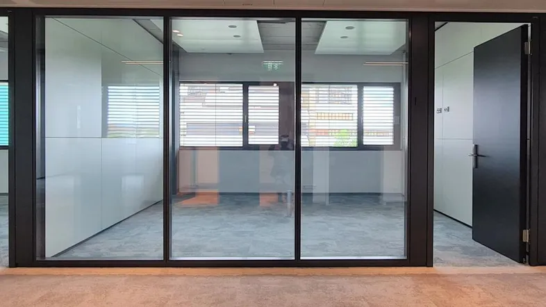 Leeres Büro mit modernen Glaswänden, Teppichboden und Fenstern mit Jalousien, bereit zur Einrichtung.