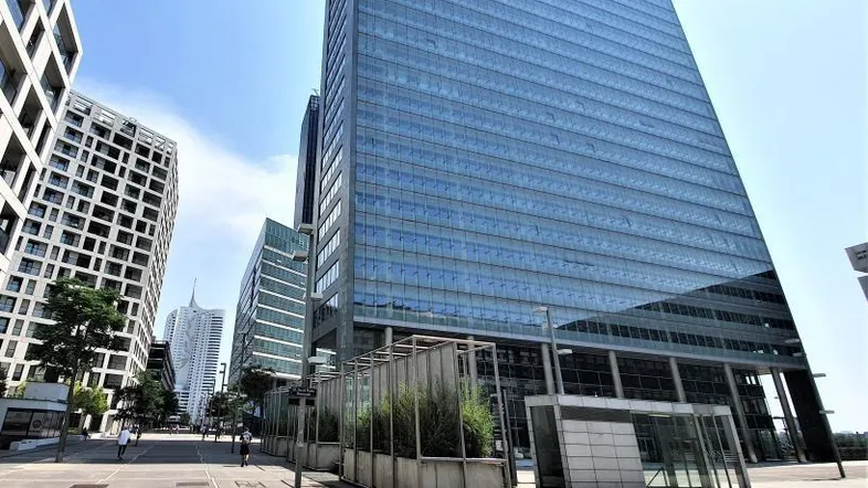 Moderne Glasfassade eines Bürogebäudes in einer städtischen Umgebung mit klarem Himmel und breitem Gehweg.