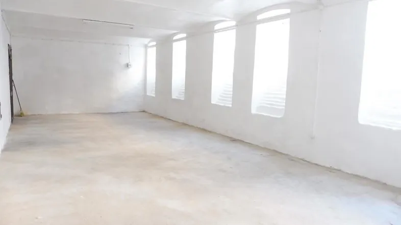 Großer, leerer Raum mit weiß gestrichenen Wänden und Betonboden, ideal für Lager oder Werkstatt.