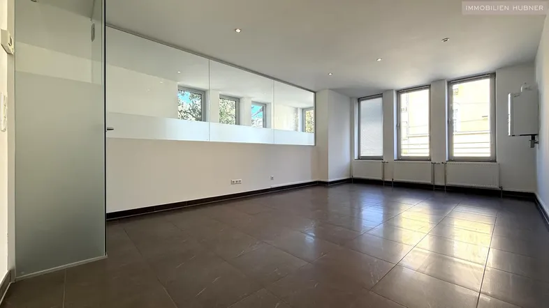 Geräumiger Büroraum mit großen Fenstern, Fliesenboden und einer modernen Glaswand.