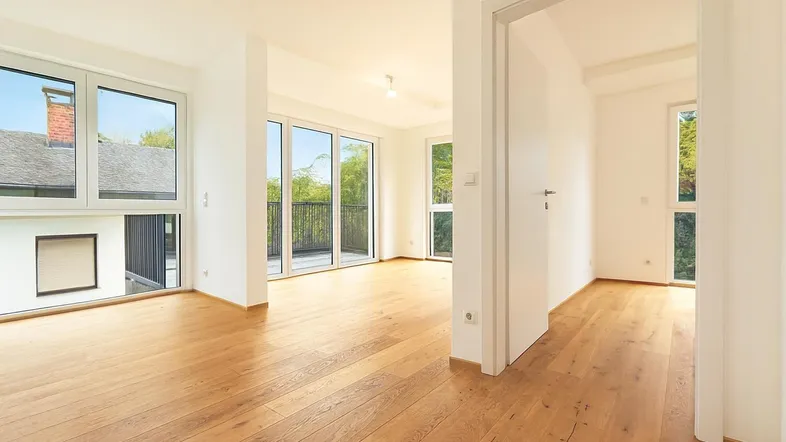 Helles, leeres Wohnzimmer mit Eichenparkettboden und Zugang zu einem Balkon.