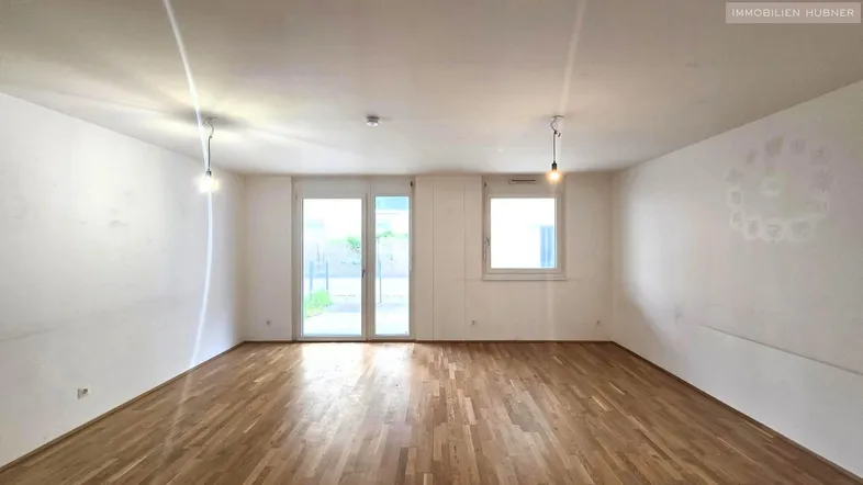 Helles Wohnzimmer mit Parkettboden und Zugang zu einem Balkon oder einer Terrasse.