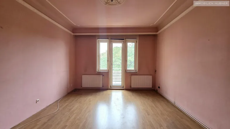 Geräumiges Zimmer mit rosa Wänden, Laminatboden und Stuckdecke, bereit zur Renovierung.