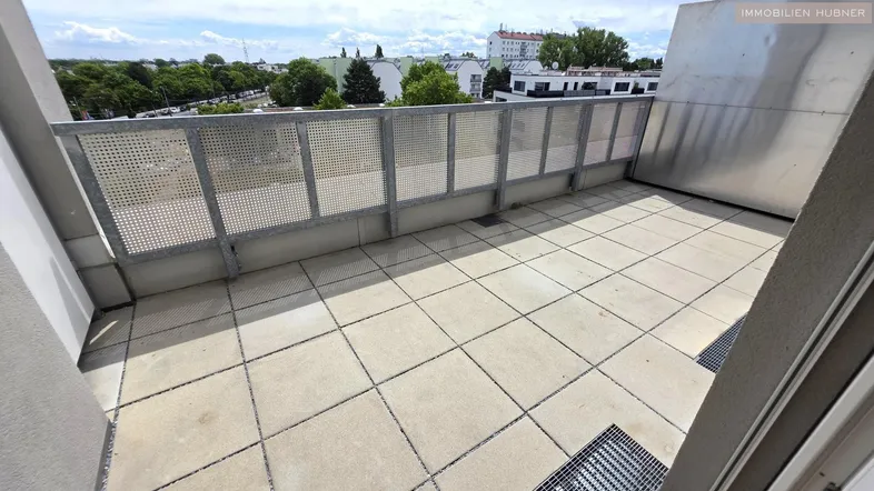 Große geflieste Terrasse mit Metallgeländer und Blick auf die Stadt unter bewölktem Himmel.