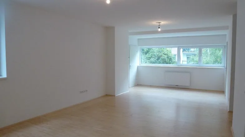 Helles, leeres Zimmer mit Parkettboden und großen Fenstern, bereit zur individuellen Gestaltung.